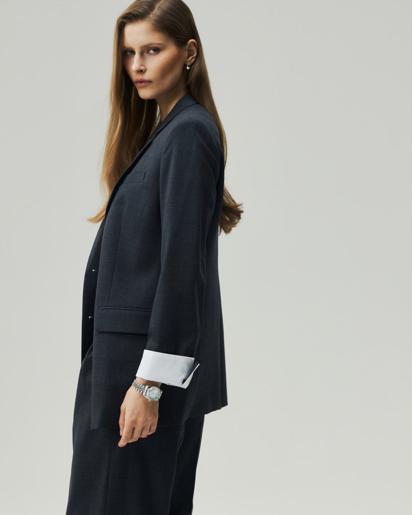 Charcoal Grey single-breasted blazer on model, side view showing the relaxed silhouette and turn-back cuff detail